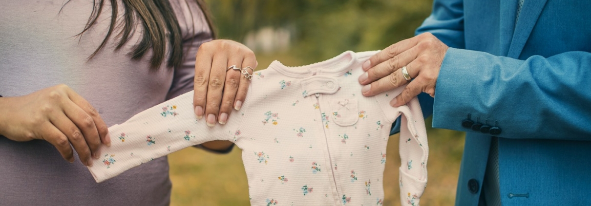 expectant parents holding baby onesie